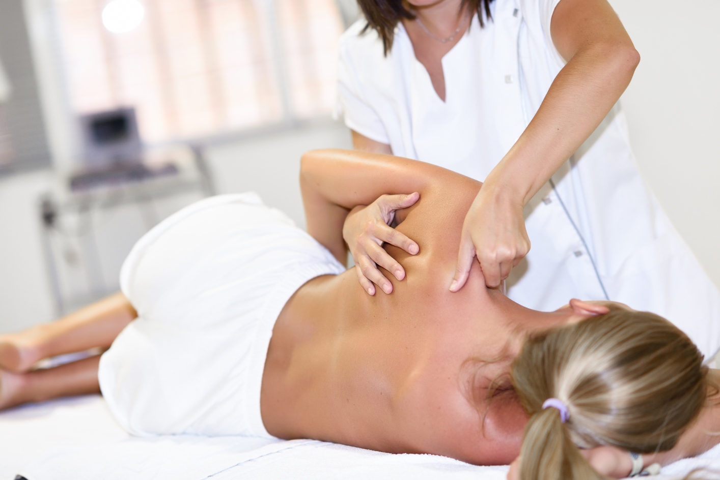 Professional female physiotherapist giving shoulder massage to blonde woman